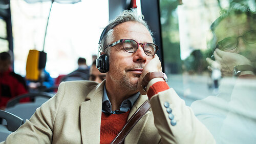 Mature tired businessman with heaphones travelling by bus in city.