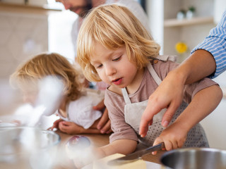 Young family with two small children indoors in kitchen, preparing food.