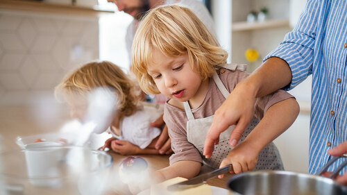 Young family with two small children indoors in kitchen, preparing food.