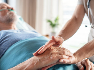 Unrecognizable female doctor examining senior man in bed in hospital.