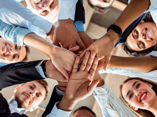 Coworkers Standing In Circle Holding Hands During Meeting In Office