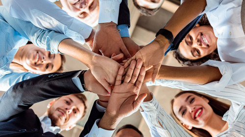Coworkers Standing In Circle Holding Hands During Meeting In Office