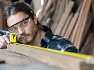 Male carpenter using measuring tape at the carpentry workshop. J