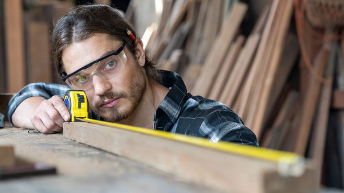 Male carpenter using measuring tape at the carpentry workshop. J