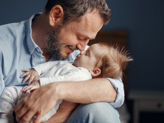 Middle age Caucasian father kissing sleeping newborn baby girl.