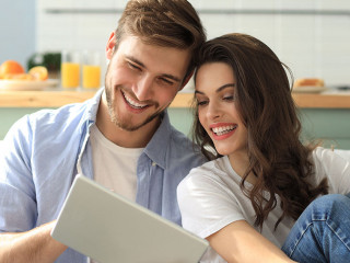 Young couple watching media content online in a tablet sitting on a sofa in the living room.