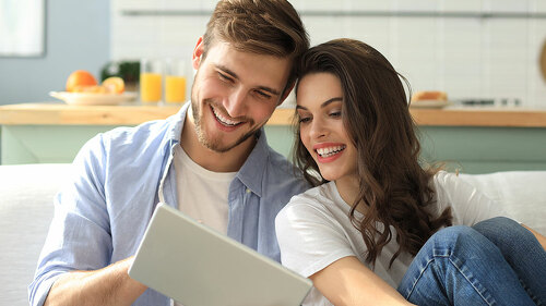 Young couple watching media content online in a tablet sitting on a sofa in the living room.