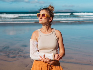 Woman with broken arm on beach. Arm cast, injured during family vacation in holiday resort. Concept of beach summer vacation.