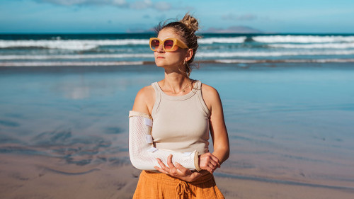 Woman with broken arm on beach. Arm cast, injured during family vacation in holiday resort. Concept of beach summer vacation.