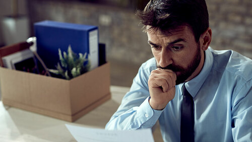 Young distraught businessman reading a notice after being fired at work,