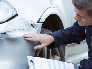 Auto Workshop Mechanic Inspecting Damage To Car And Filling In R