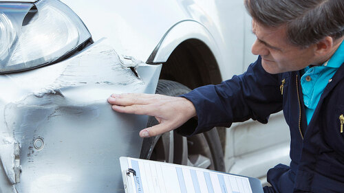 Auto Workshop Mechanic Inspecting Damage To Car And Filling In R