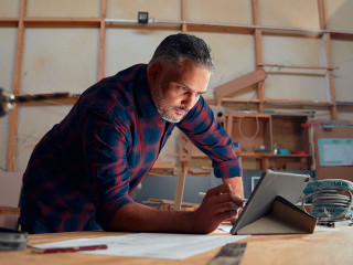 Mid adult man writing with digitized pen on digital tablet next to tools in woodworking factory