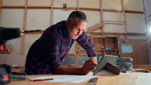 Mid adult man writing with digitized pen on digital tablet next to tools in woodworking factory