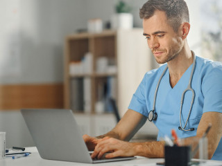 Experienced Male Nurse Wearing Blue Uniform Working on Laptop Co