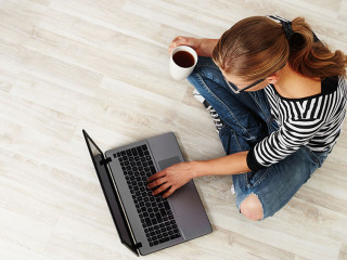 Young woman with coffee mug sitting on the floor with laptop. Co