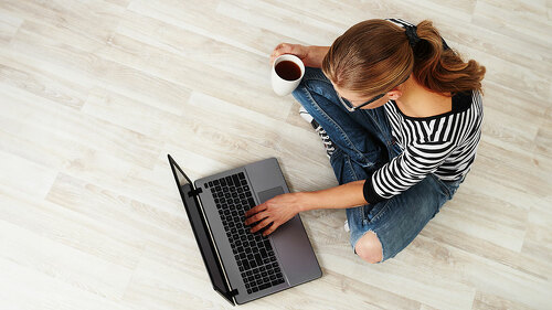Young woman with coffee mug sitting on the floor with laptop. Co