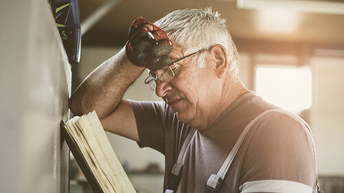 Senior man in workshop. Worried man reading his planner.