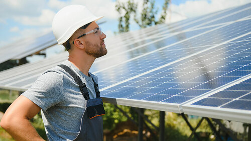 Male engineer in protective helmet installing solar photovoltaic panel system. Alternative energy ecological concept.