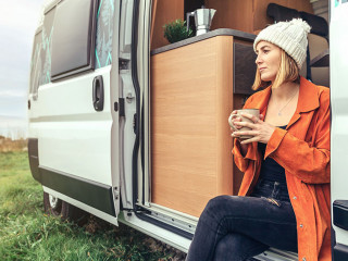 Woman drinking coffee sitting at the door of a campervan