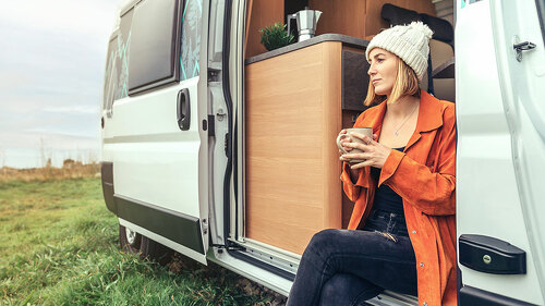 Woman drinking coffee sitting at the door of a campervan