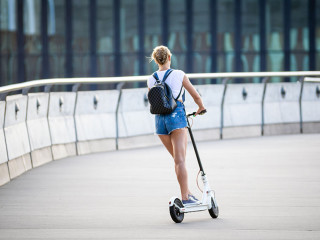 Back view of woman riding an electric scooter on modern buildings background