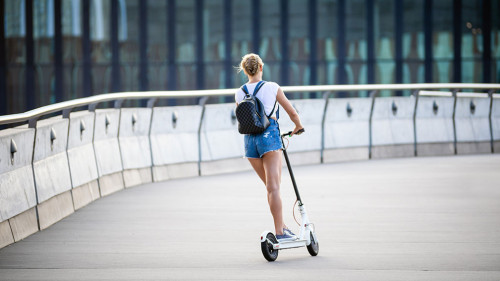 Back view of woman riding an electric scooter on modern buildings background