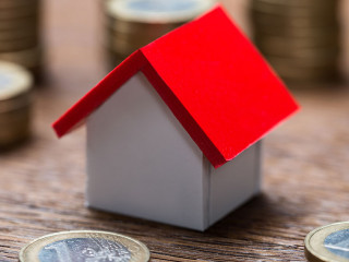 House Model Amidst Coins At Table