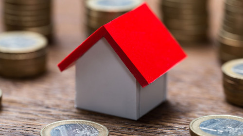 House Model Amidst Coins At Table