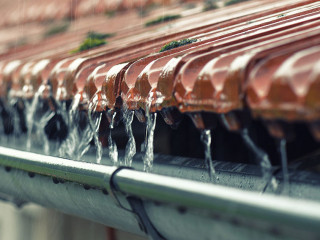 Drops of water flow into the eaves on the house in the rain.