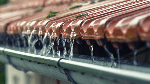 Drops of water flow into the eaves on the house in the rain.