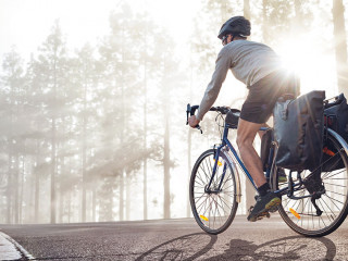 Cyclist on a bicycle with panniers riding along a foggy forest r