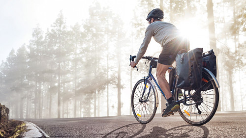 Cyclist on a bicycle with panniers riding along a foggy forest r