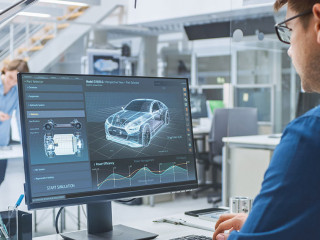 Over the Shoulder Shot of Engineer Working with CAD Software on Desktop Computer, Screen Shows Technical Drafts and Drawings. In the Background Engineering Facility Specialising on Industrial Design