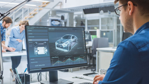 Over the Shoulder Shot of Engineer Working with CAD Software on Desktop Computer, Screen Shows Technical Drafts and Drawings. In the Background Engineering Facility Specialising on Industrial Design