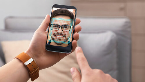 Man using smartphone with facial recognition system indoors, clo