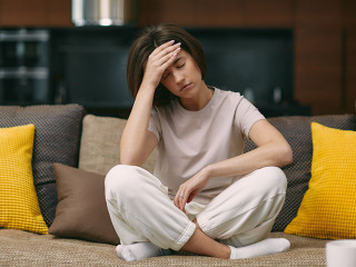 Sick young girl suffering headache or migraine, sitting on sofa at home, feel pain of sore head, morning after hangover