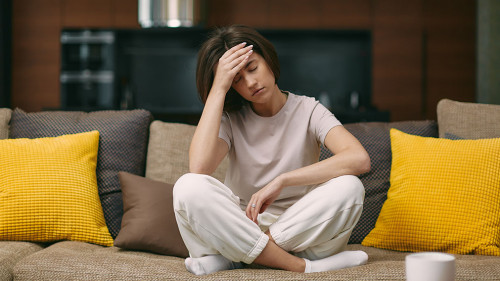 Sick young girl suffering headache or migraine, sitting on sofa at home, feel pain of sore head, morning after hangover