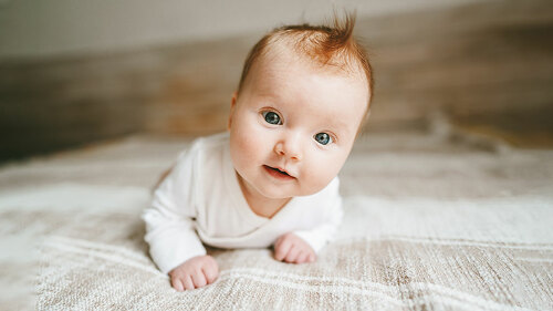 Cute baby ginger hair close up crawling on bed smiling adorable kid portrait family lifestyle 3 month old child