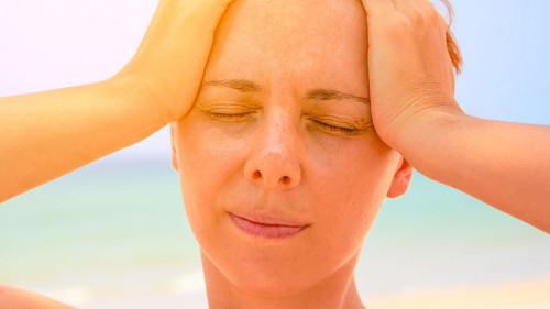 Young woman suffering with headache. Woman on hot beach with sunstroke. Health problem on holiday.