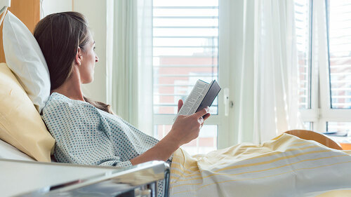 Patient in hospital room looking out of the window from bed
