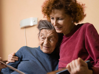 Senior woman and her adult daughter looking at photo album together on couch in living room, talking joyful discussing memories. Weekend with parents, family day, thanksgiving, mom's holiday