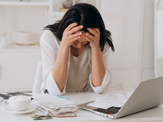 Desperate young woman holds head in hands, feeling overwhelmed by financial paperwork at white office desk, struggling with bills, taxes, and credit management, bankruptcy concept, mental health