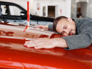 Man lying on the hood of new car in showroom
