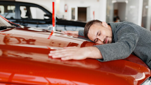 Man lying on the hood of new car in showroom
