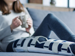 Smiling brunette girl with broken leg is sitting on couch sofa,