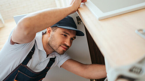 Hardworking plumber look under sink in kitchen. He put new hose under it. Wrench lying on desk.