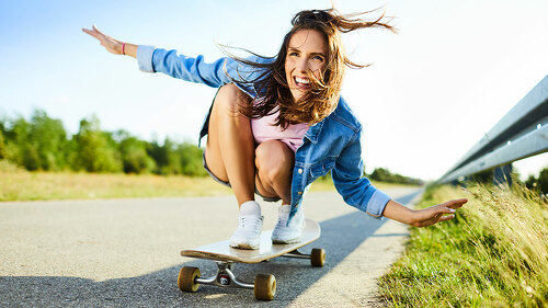 Cheerful young woman riding longboard in countryside setting