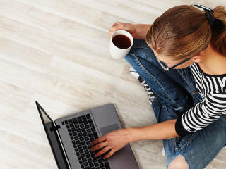 Young woman with coffee mug sitting on the floor with laptop. Co