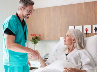 Surgeon Visiting And Shaking Hands With Mature Female Patient In Hospital Bed